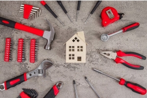 Kit de herramientas de bricolaje con martillo, destornilladores, alicates y llaves alrededor de una maqueta de una casa