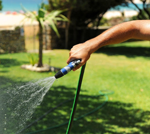 Mano sosteniendo una manguera de jardín mientras riega
